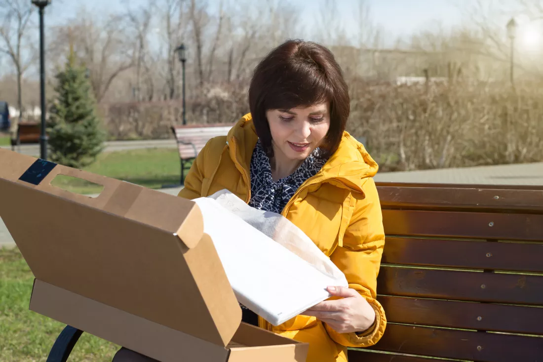 happy-brunette-woman-bright-yellow-jacket-bench-with-smile-opens-box-with-new-laptop